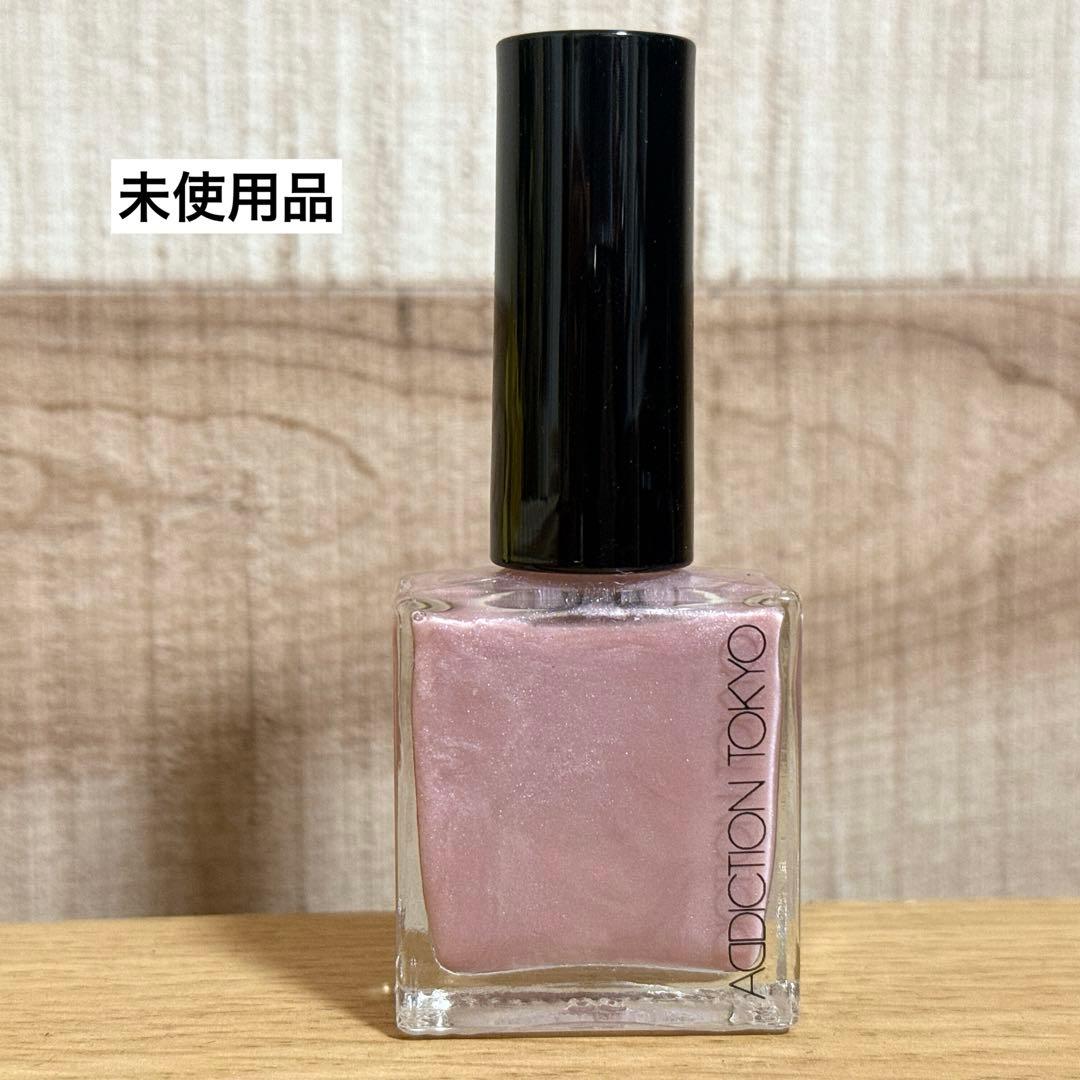 A bottle of Addiction nail polish in a shimmery light pink shade sitting on a wooden surface.