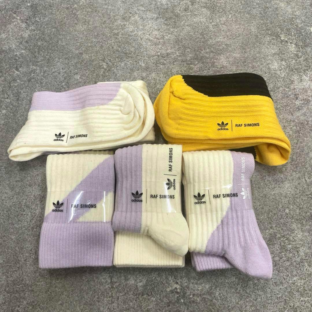 Five adidas RAF SIMONS socks, mostly lavender with one yellow pair, laid flat on a gray surface.