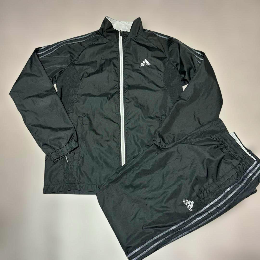 Black adidas CLIMAPROOF windbreaker jacket and matching pants laid flat on a light background.