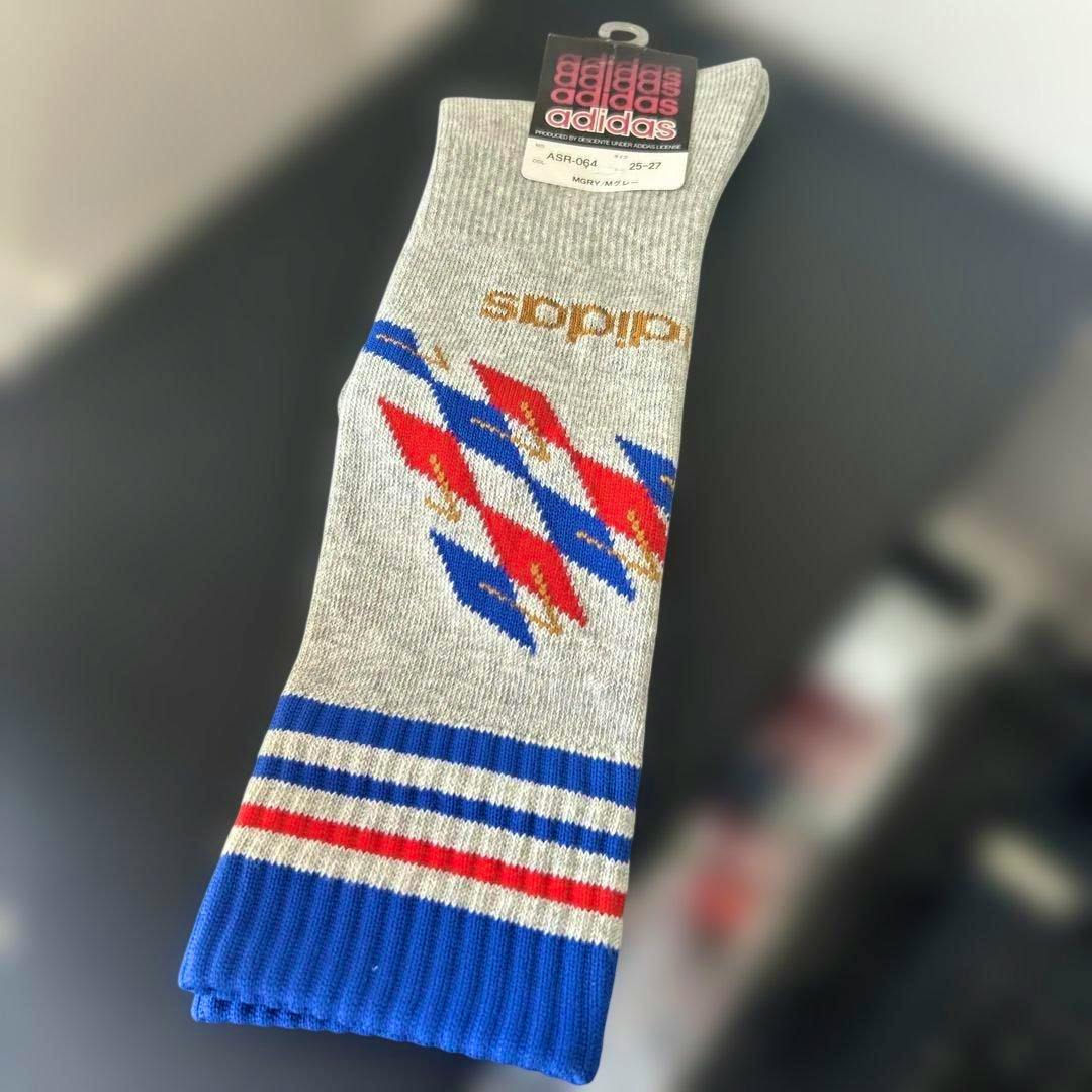 Grey adidas crew sock (men's, 25–27 cm) with blue and red pattern and a brand hang tag visible.