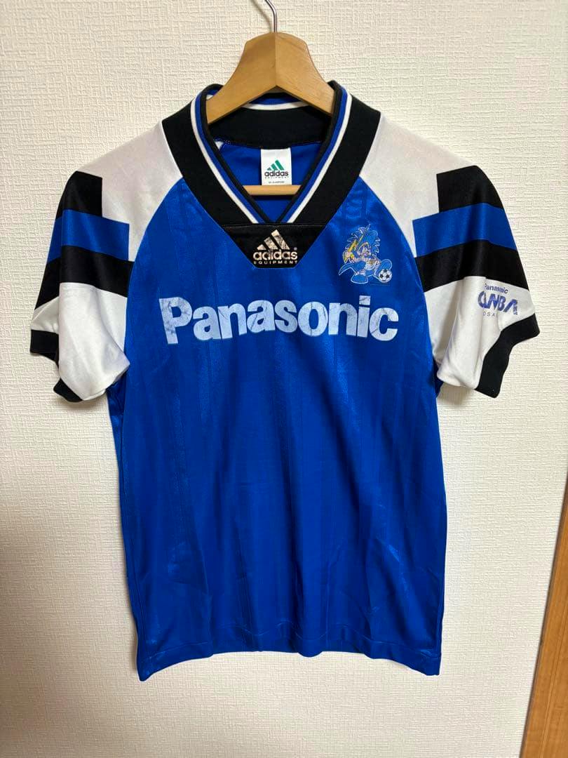 Front view of an adidas EQUIPMENT ガンバ大阪 blue polyester jersey with Panasonic sponsor logo and club crest hanging on a hanger.