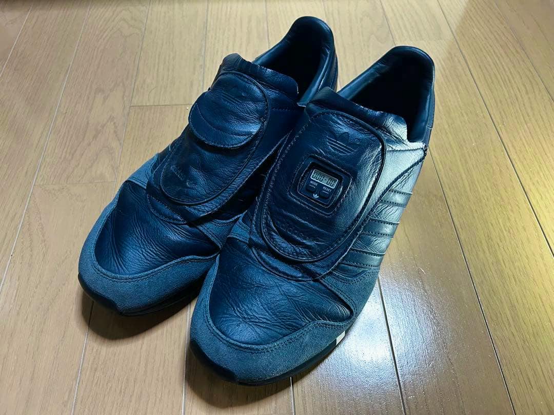 Pair of black adidas HYKE Micro Pacer leather sneakers displayed on a wooden floor.
