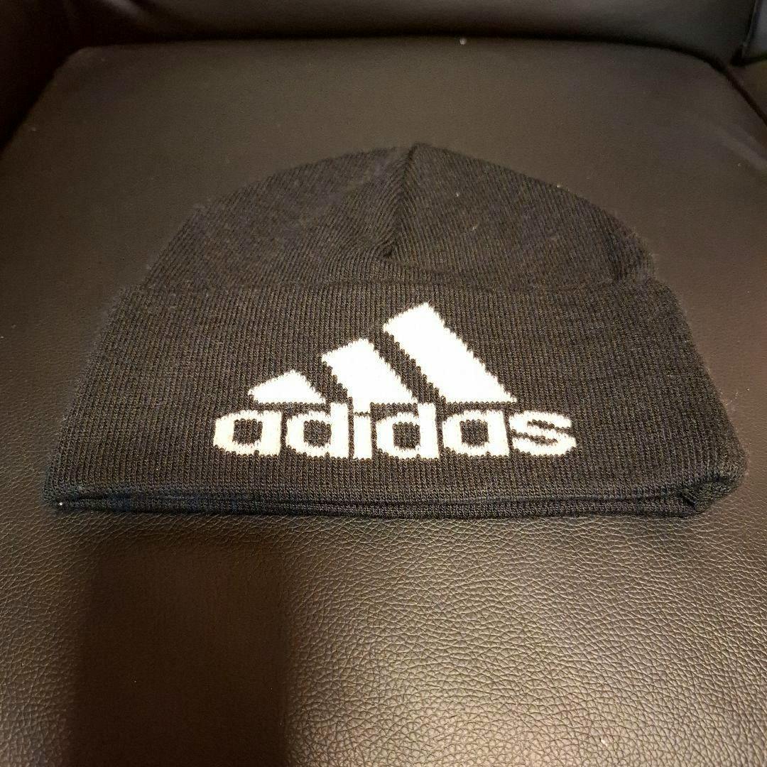 Black adidas knit beanie with a white adidas logo on the cuff laid flat on a dark surface.