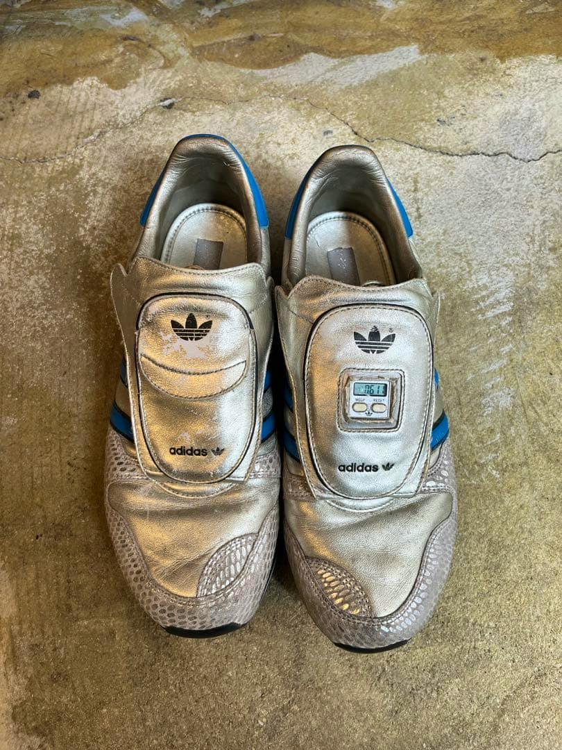 Top-down photo of a pair of silver adidas Micro Pacer sneakers (2008 reissue) showing both shoes with blue stripes.