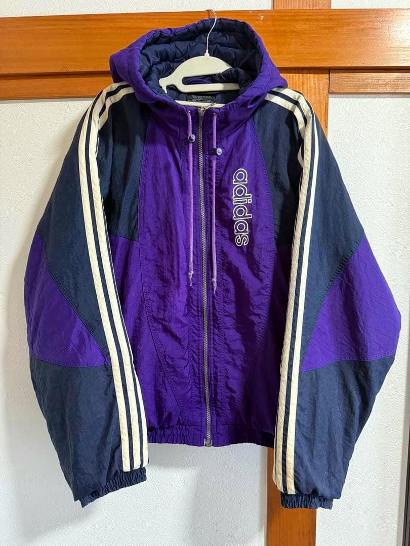 Front view of a purple adidas nylon hooded jacket with a center zipper, white three-stripes on the sleeves, and a vertical adidas logo.