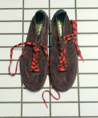 Top-down photo of a pair of adidas Samba Decon leather sneakers with red-and-black laces placed on a tiled floor.