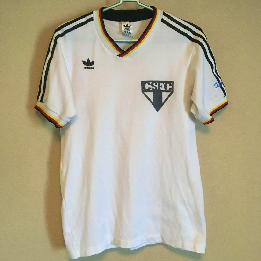 White adidas soccer jersey with black three-stripe shoulders, multicolor sleeve trim, and a CSFC crest on the chest, hanging on a hanger.