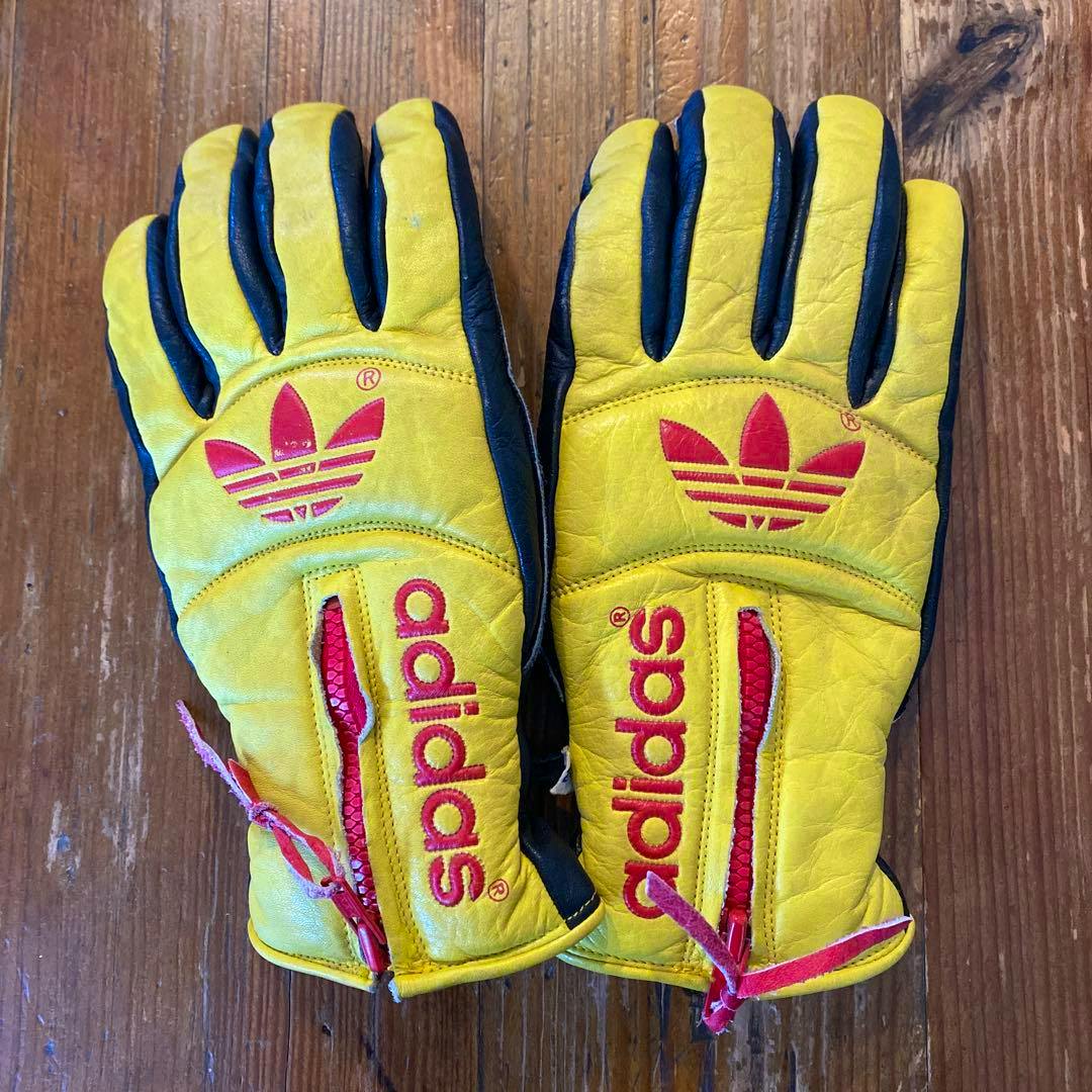 A pair of vintage yellow and black adidas leather gloves with red trefoil logos laid flat on a wooden surface.