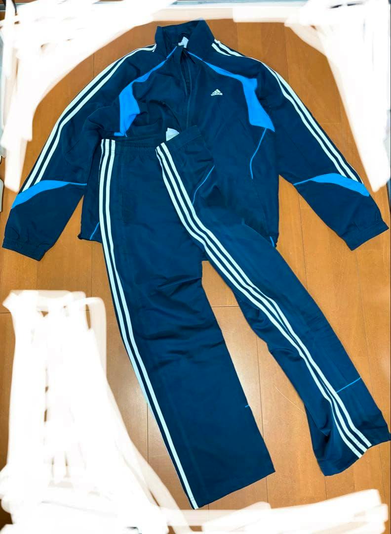Navy adidas windbreaker jacket and matching track pants laid flat on a wooden floor, showing the three stripes and adidas logo.