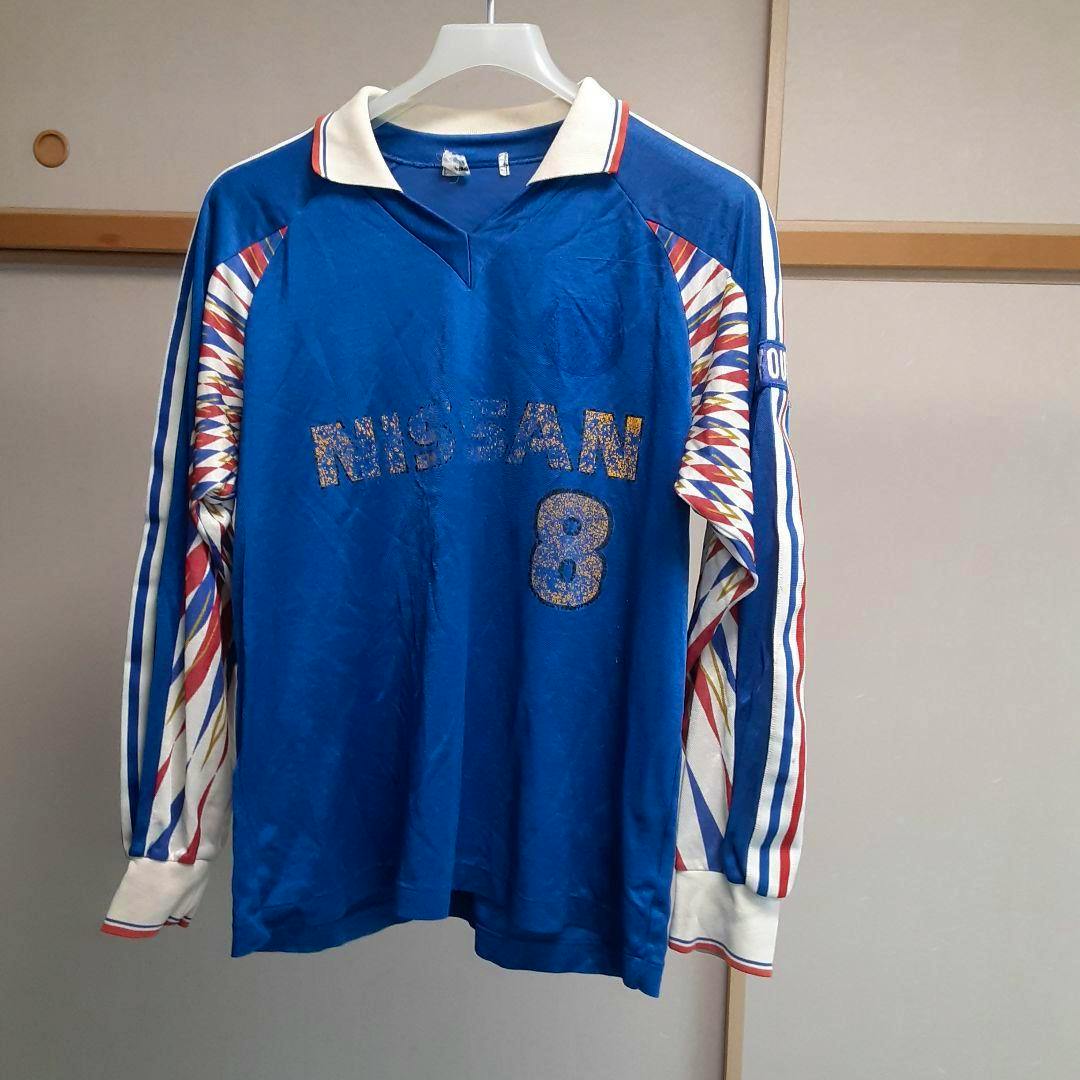 Blue Yokohama Marinos polyester T-shirt with a white collar, patterned long sleeves, and 'NISSAN' with the number 8 printed on the front, hanging on a hanger.