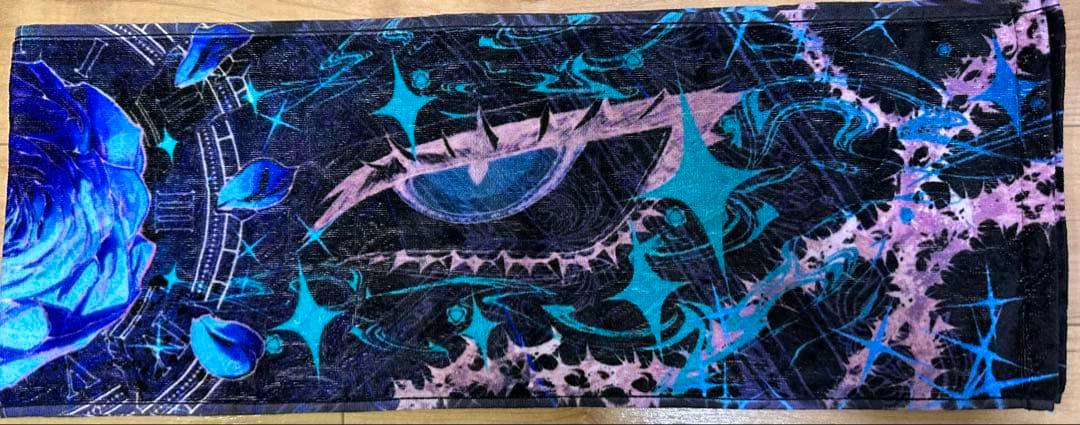 Rectangular muffler towel laid flat showing a blue rose and abstract eye-shaped teal and purple pattern on a black background.