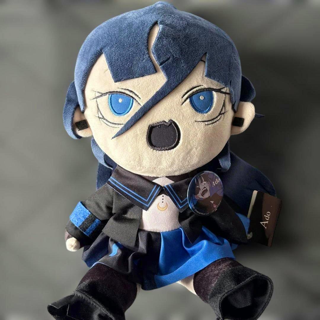 Front view of the Ado ぬいぐるみ うっせぇわ plush wearing a blue-and-black outfit with a round pin attached.