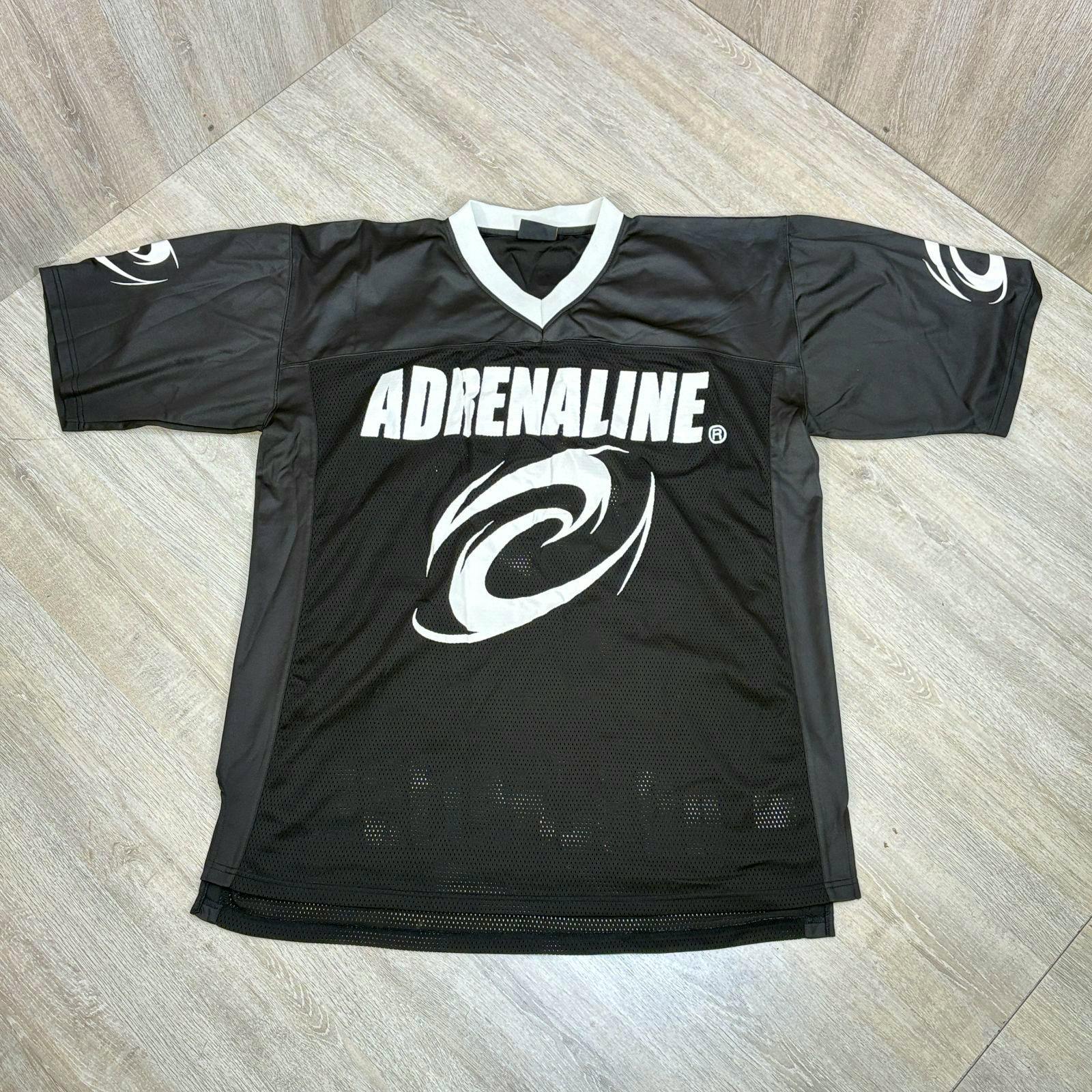 Black ADRENALINE mesh hockey-style jersey with white logo and swirl graphic laid flat on a wood floor.
