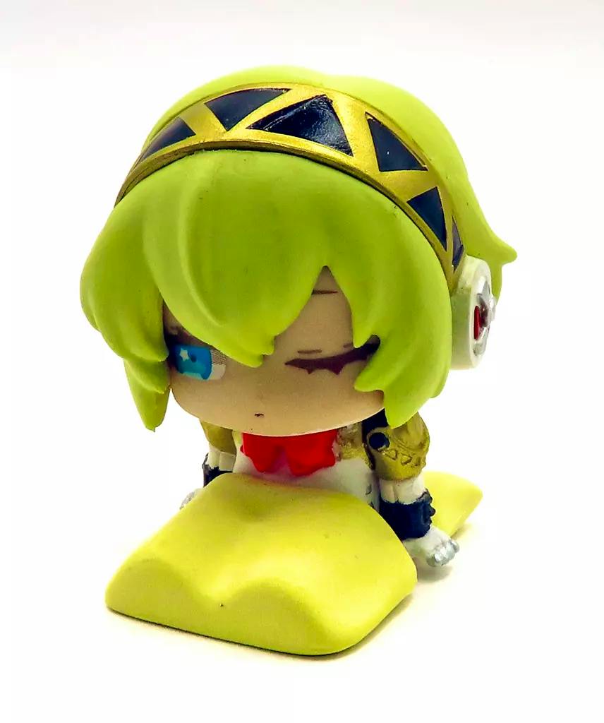 Front view of a small chibi trading figure of Aigis from Persona 3 resting on a yellow cushion against a white background.