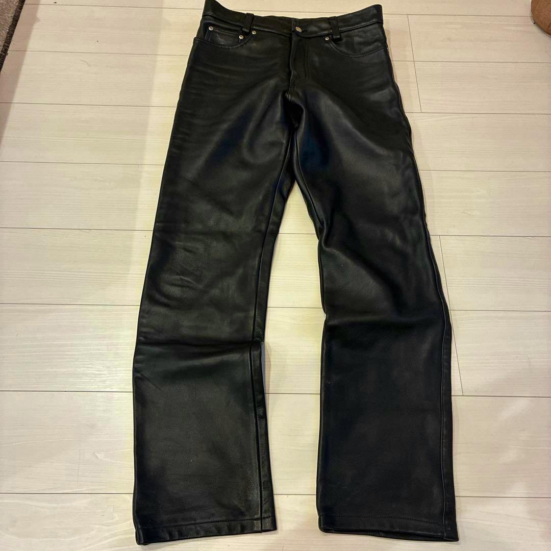Black steerhide leather pants laid flat on a light wood floor.