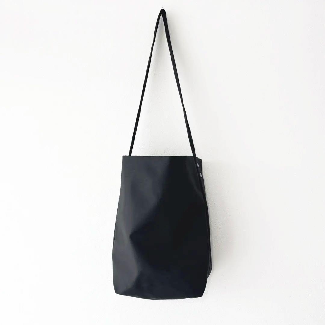 Black nylon shoulder bag hanging from its strap against a white wall.