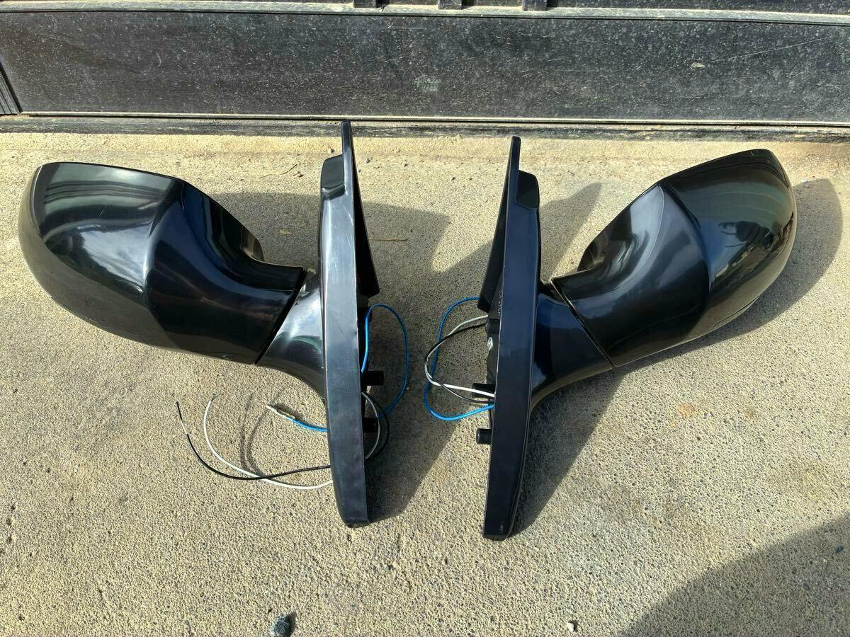 Pair of black aftermarket car door mirrors with visible wiring and LED turn signal housings laid on concrete.