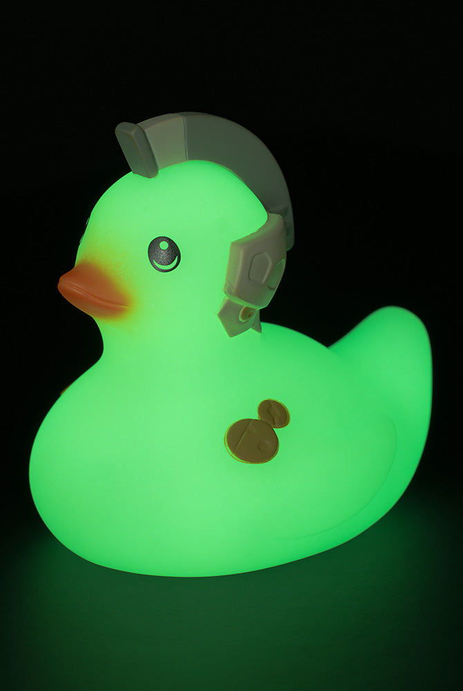 A glow-in-the-dark duck-shaped desk lamp wearing a gray helmet, glowing green against a black background.