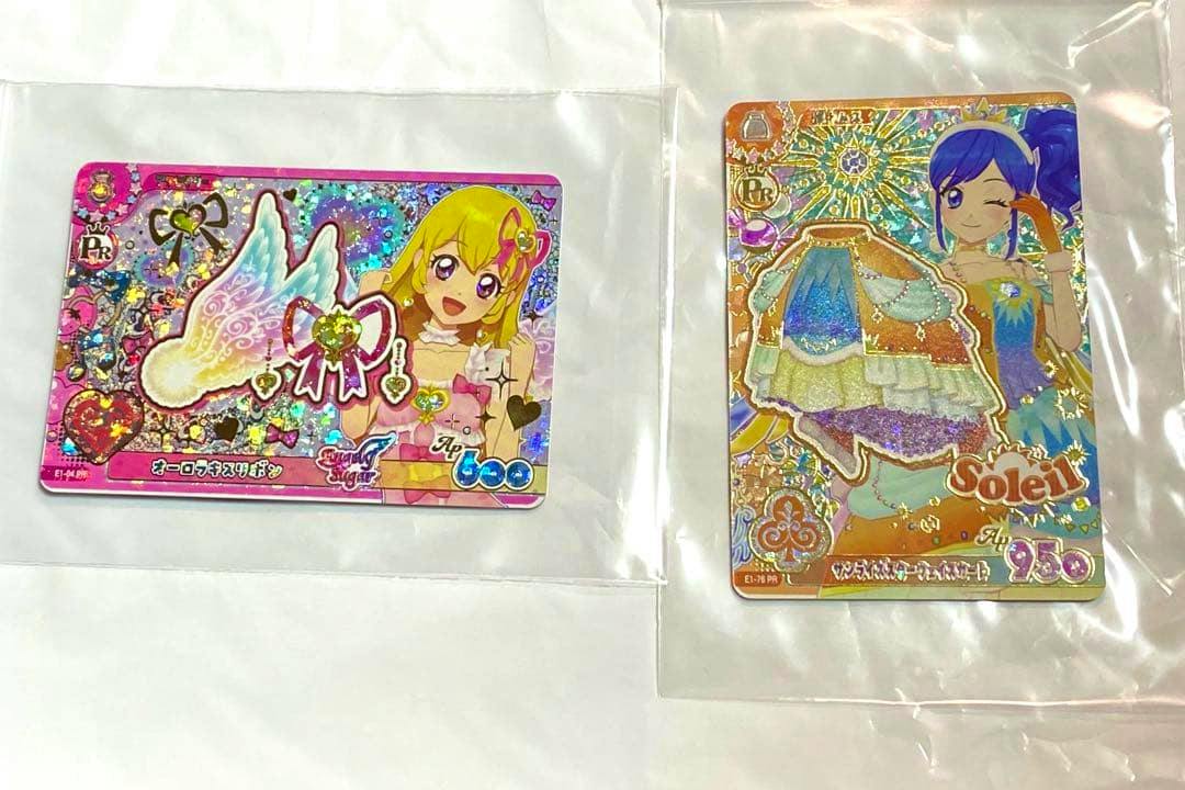 Photo of two Aikatsu paper cards (オーロラキスリボン and サンライズスターウェイスカート) in plastic sleeves on a white background.