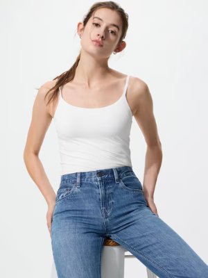 Model wearing a white Airism bra camisole tucked into blue jeans while seated.