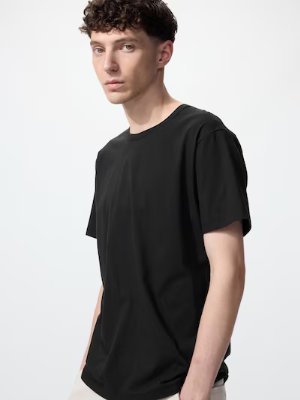A male model wearing the product, a black men's oversized Airism cotton T-shirt with mid-length sleeves.