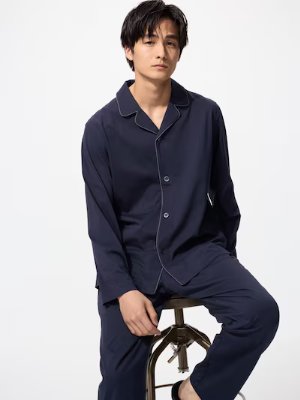 A man wearing navy men's cotton pyjamas seated on a stool against a white background.