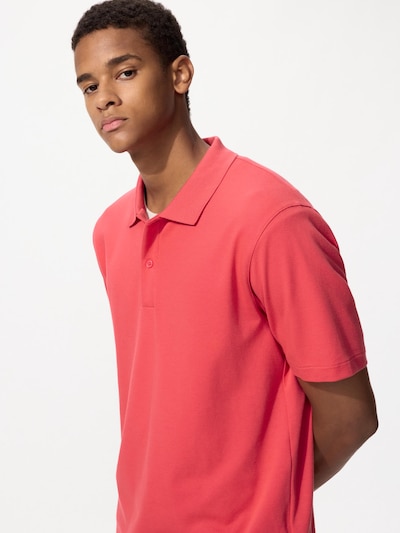 Male model shown from the torso up wearing a coral cotton polo shirt.