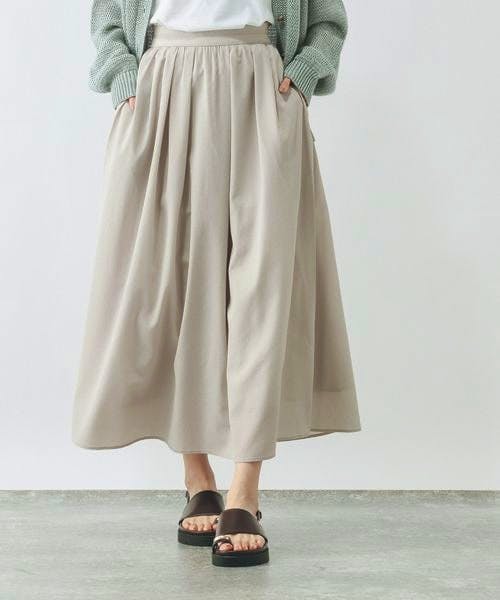 Model wearing a light beige flared women's skirt with a gathered waist and midi length.