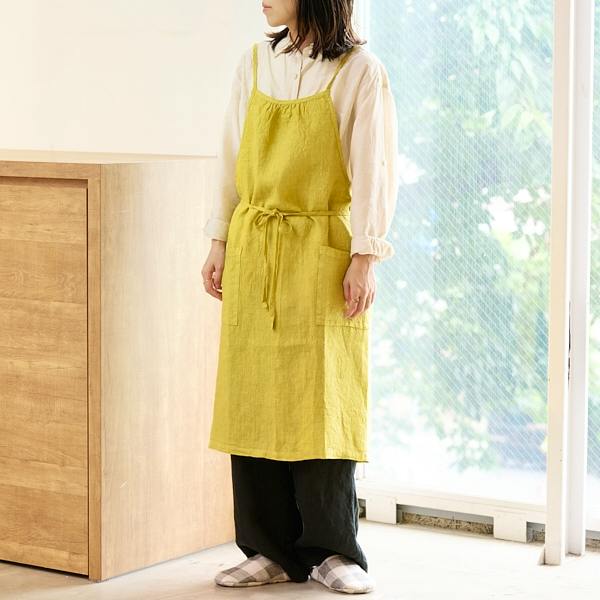 A model wearing the AKOMEYA TOKYO mimosa apron standing indoors, showing the front view of the apron.