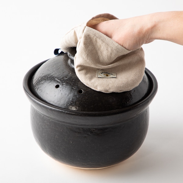 A natural-colored cotton-linen pot holder being used to lift the lid of a black rice pot.