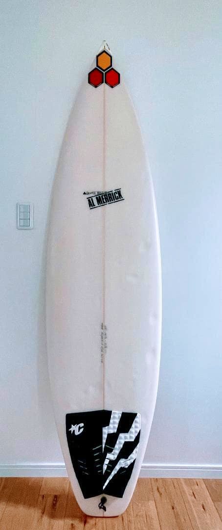 Front view of an AL MERRIC Flyer F 6'2" surfboard standing upright against a white wall.