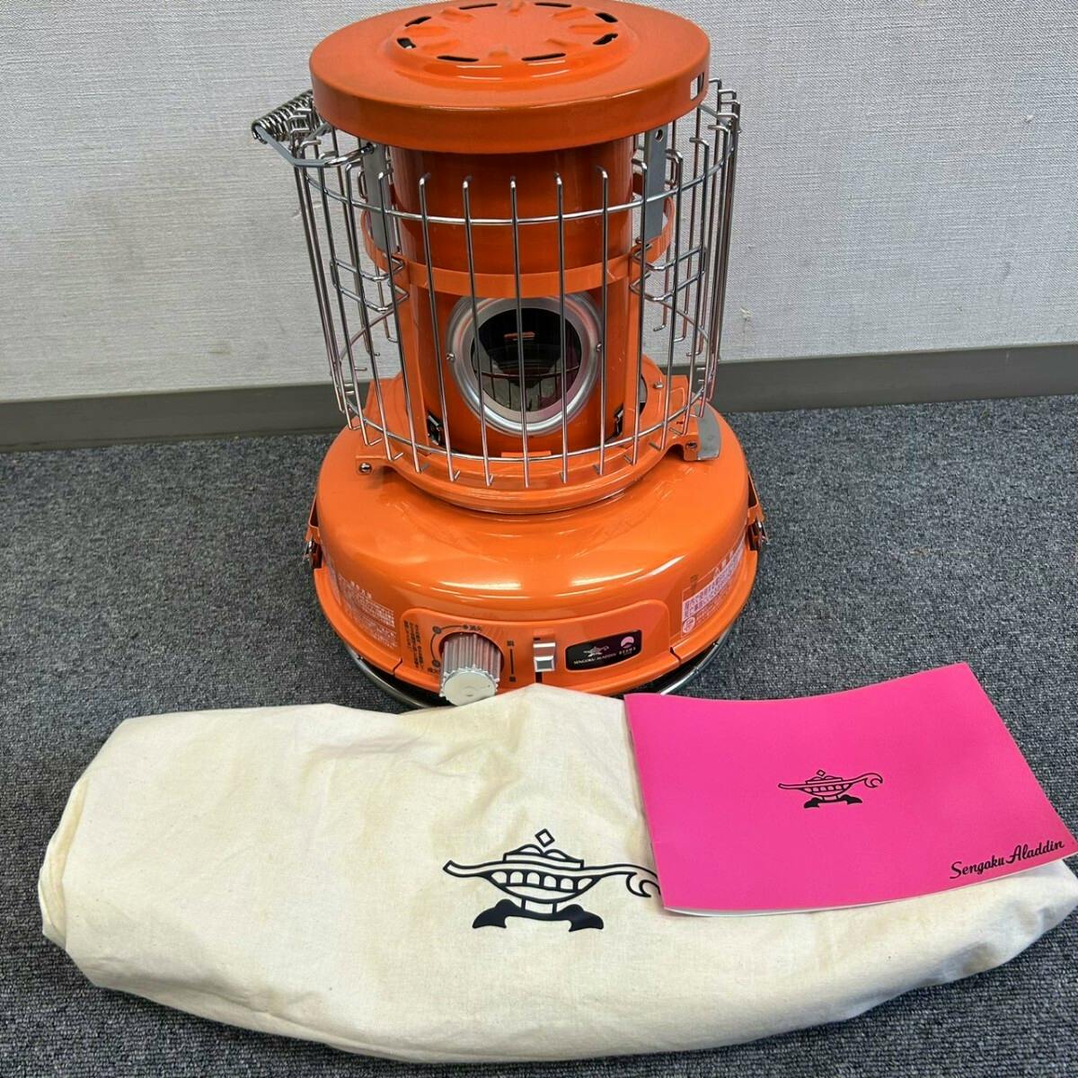 Orange Aladdin portable gas stove (SAG-BF01) shown with its canvas carrying bag and pink manual in front.