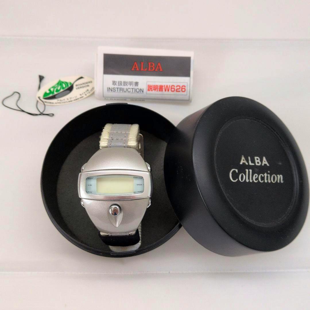 A digital ALBA SPOON wristwatch with its strap displayed in an open round ALBA Collection box, with the instruction booklet and tag visible nearby.