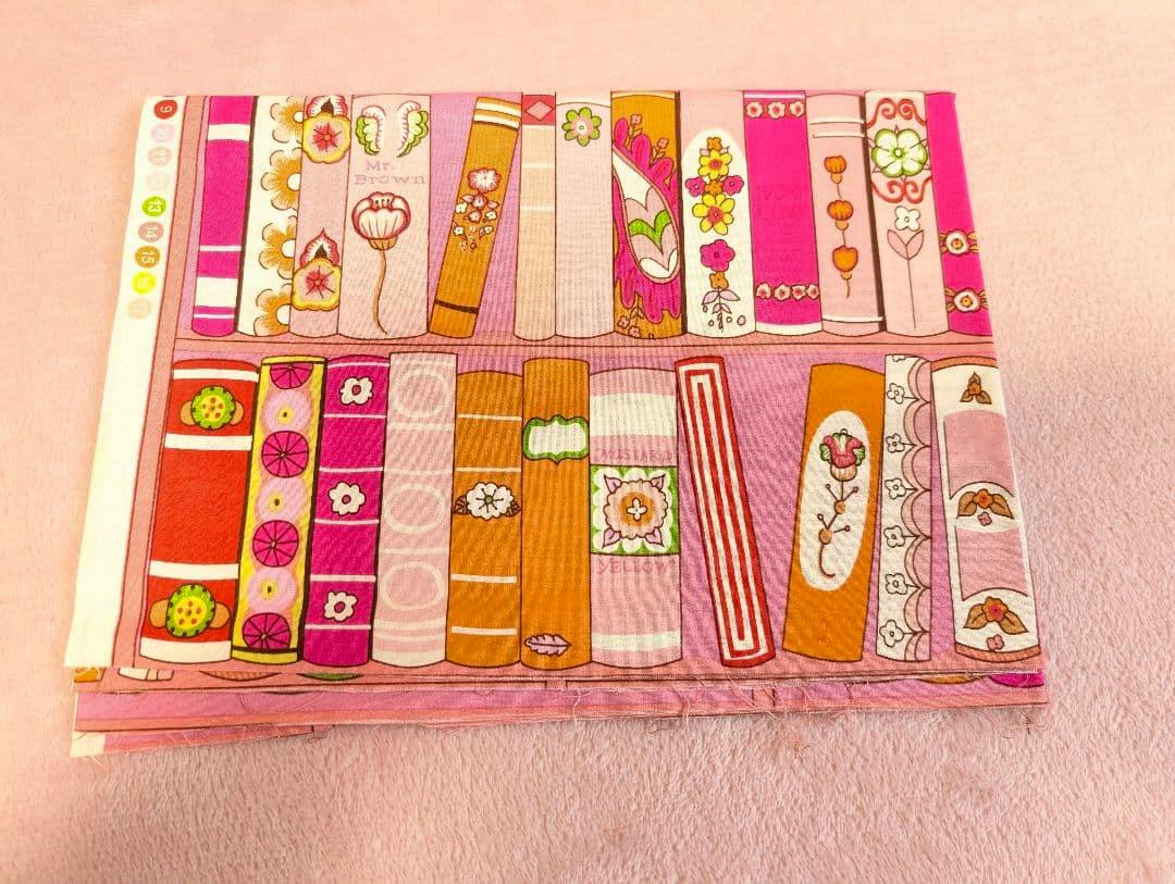 Folded Alexander Henry cotton fabric showing a pink illustrated bookshelf/book-spine print on a pale pink surface.