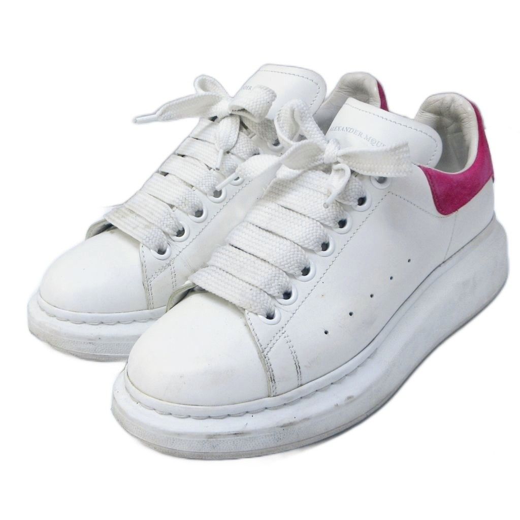 Pair of white Alexander McQueen oversized leather low-top sneakers with pink heel tabs shown at an angle.