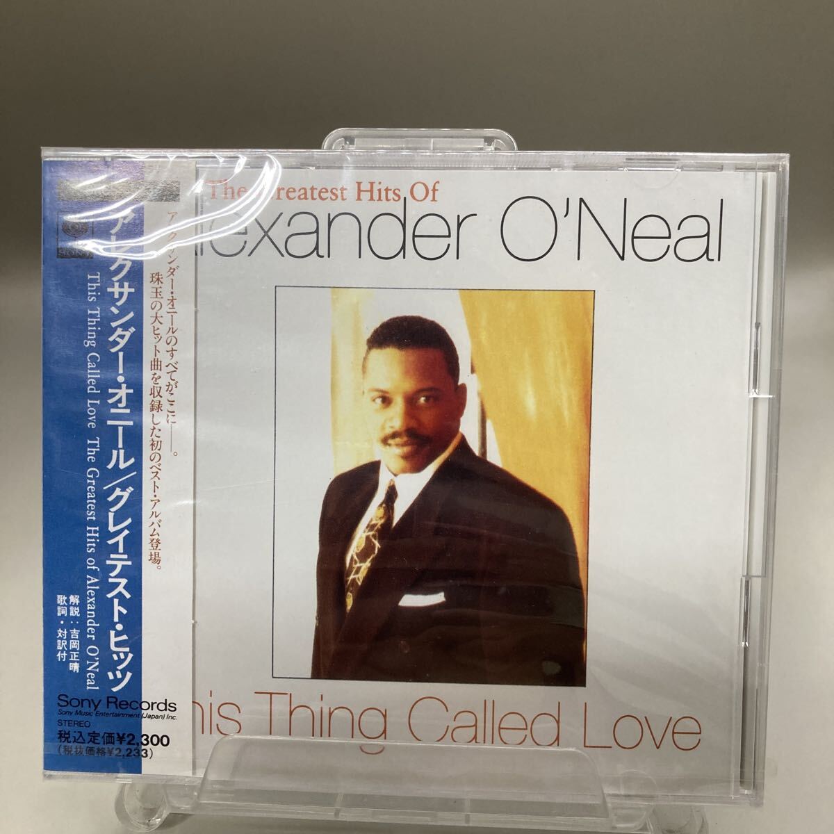 Front of a sealed CD case for Alexander O'Neal "This Thing Called Love: The Greatest Hits Of Alexander O'Neal" with a Japanese obi sash visible.
