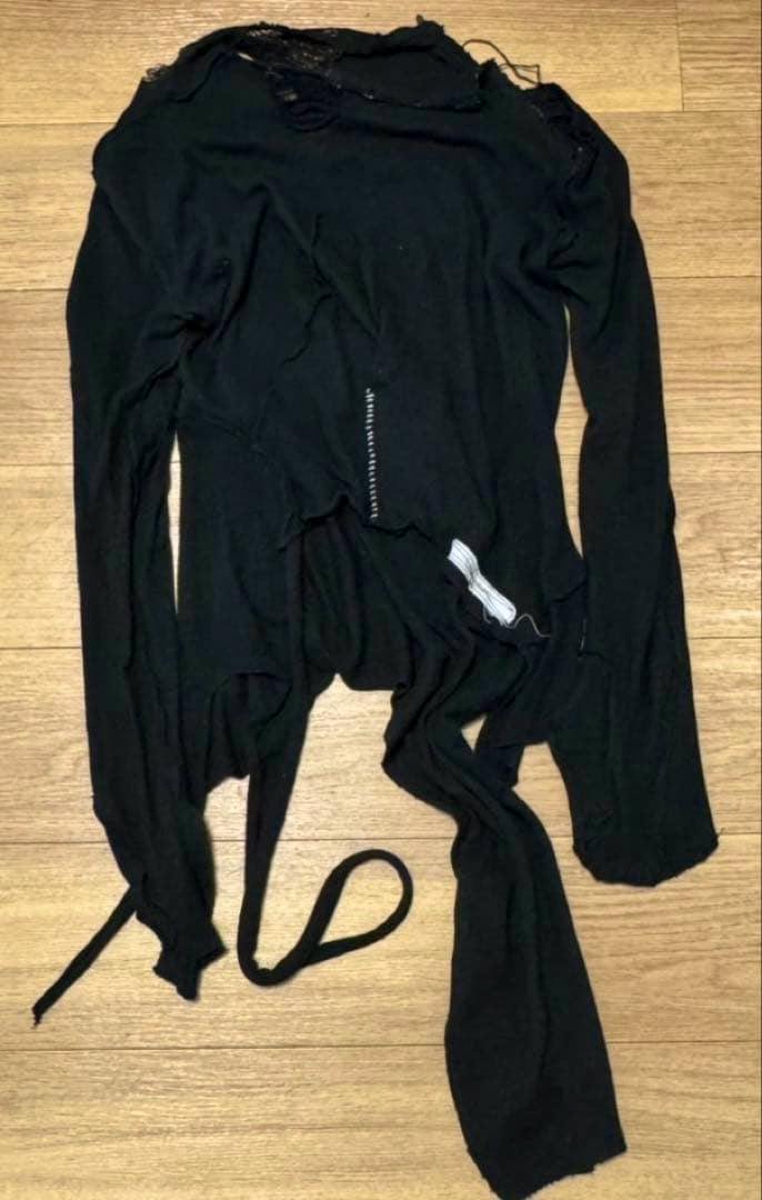 Black long-sleeve wool sweater with an asymmetric hem laid flat on a wooden floor.