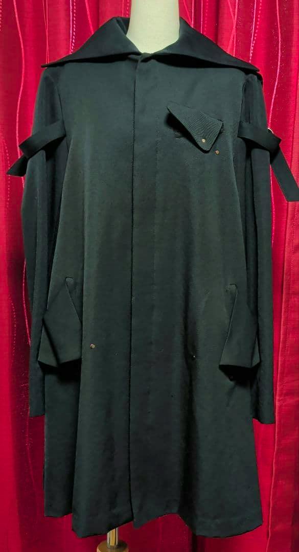 Front view of a black women's coat on a dress form against a red curtain.