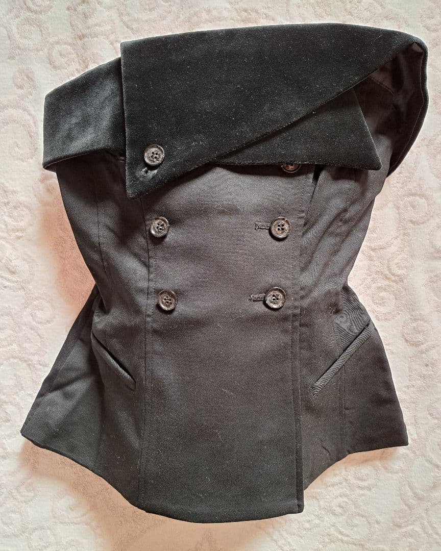 Black corset with double-breasted button front and wide folded collar laid flat on a patterned surface.