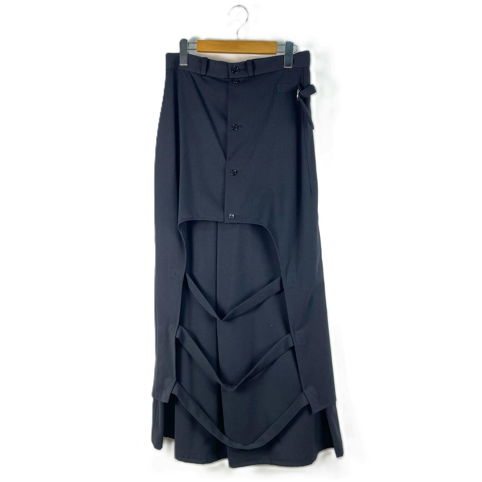 Black wrap skirt with buttoned front and layered strap detailing hanging on a hanger against white background.
