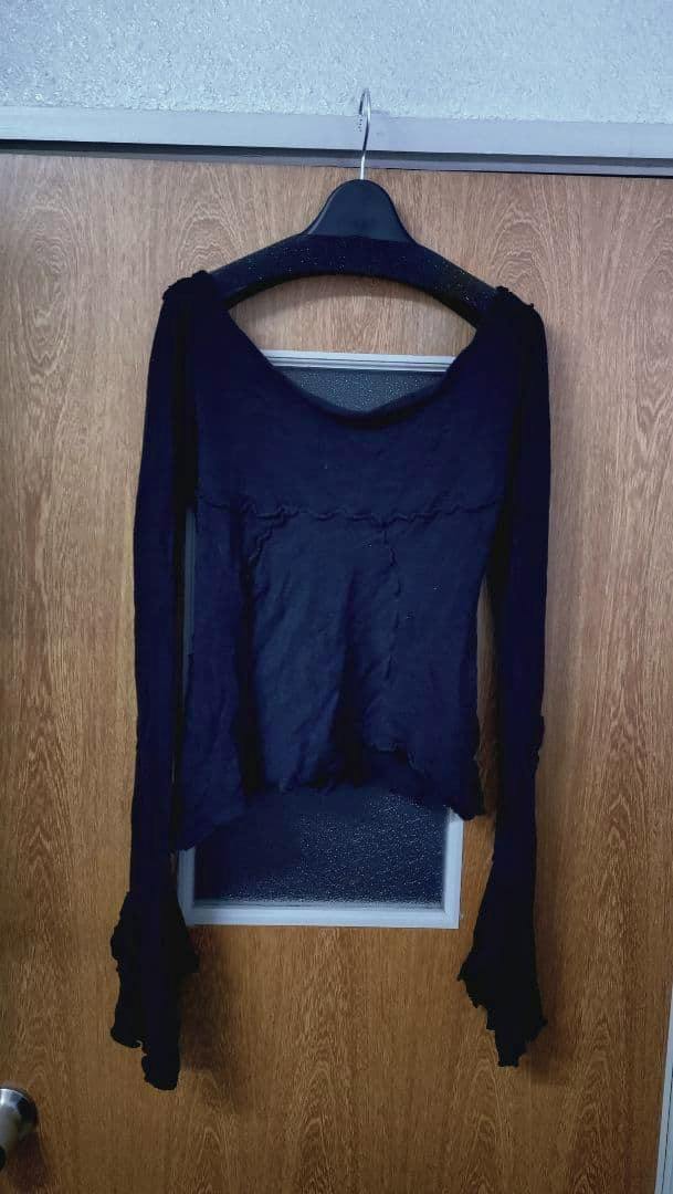 Black long-sleeve cotton cut‑and‑sew top hanging on a hanger against a wooden door.