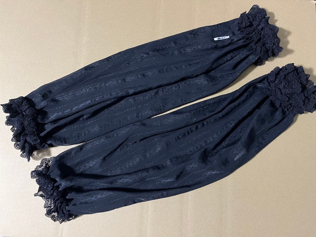 A pair of black alice auaa polyester arm covers with lace ruffled ends laid flat on a beige surface.