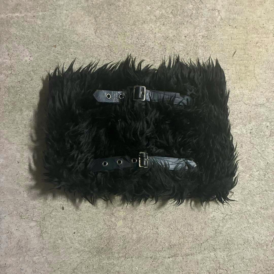 Black polyester neck warmer with two buckle straps laid flat on a textured surface.