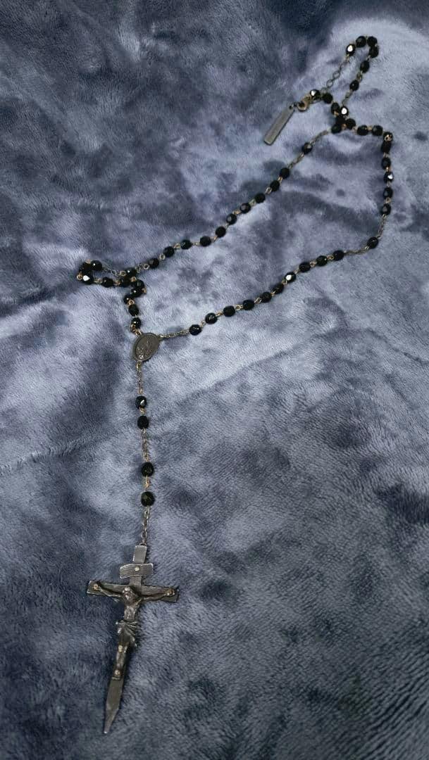 A rosary necklace (alice auaa ロザリオ) with black beads and a crucifix laid out on a gray plush surface.