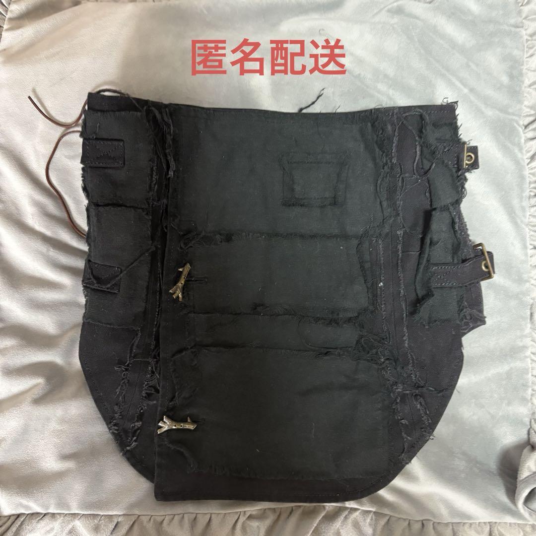 Flat-lay photo of a black corset with frayed edges and metal hooks on a gray surface.