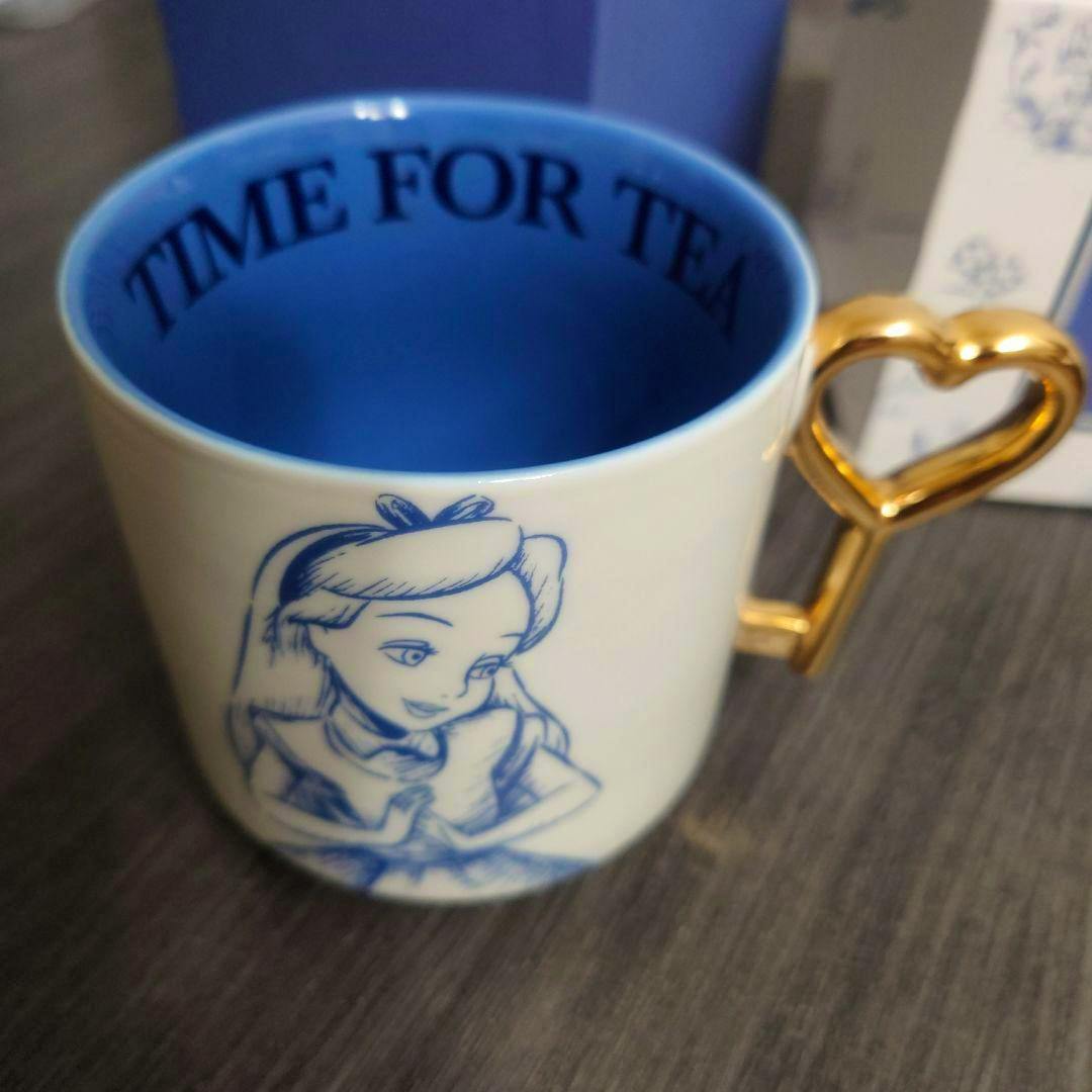 Alice in Wonderland mug showing a blue interior, an Alice illustration on the outside, and a gold heart-shaped handle.