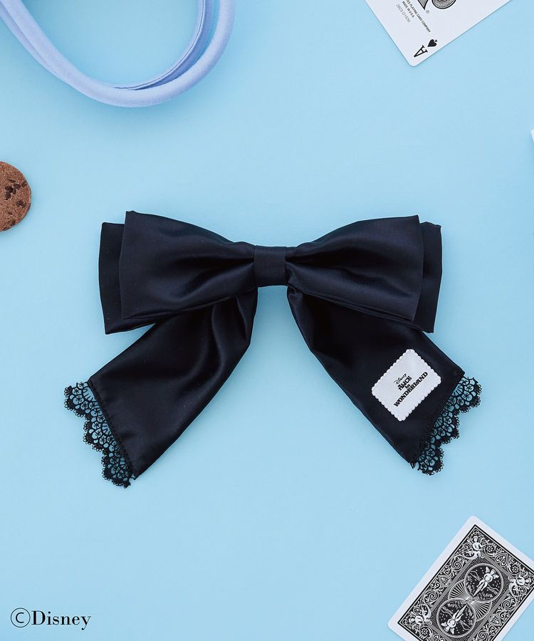 Black ribbon barrette with lace-trimmed tails and a small label laid flat on a blue background.