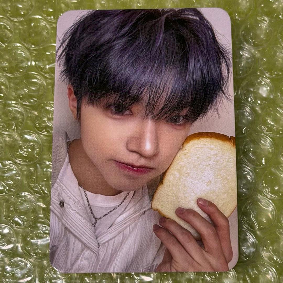 Photocard showing a close-up of a person with dark hair holding a slice of bread on a bubble-wrap background.