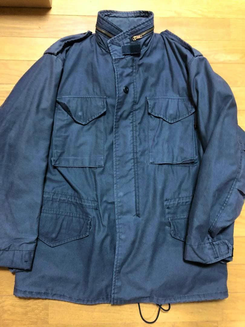Front view of a black Alpha Industries M-65 field jacket laid flat on a wooden floor.