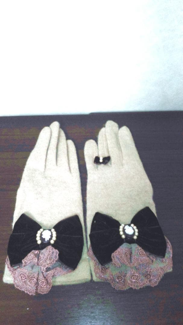 Beige gloves (Amavel) with cameo ribbon bows and lace cuffs laid flat on a dark surface.